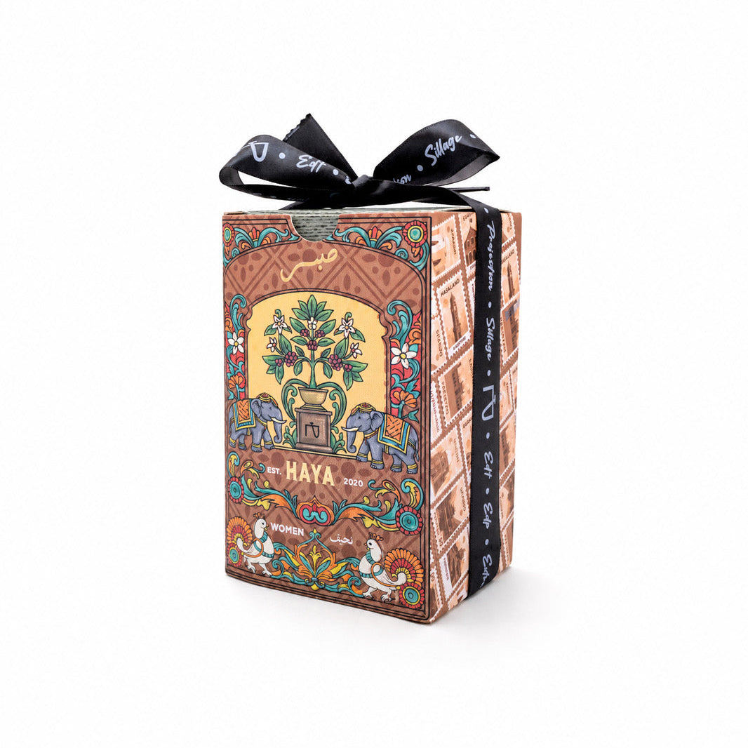 A rectangular decorative box with an ornate multicolor illustration and the word 'HAYA' on the front, tied with a black ribbon bow, photographed on a clean white background.